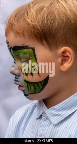 Das Gesicht eines hellhaarigen Jungen aus Nahaufnahme mit grüner Farbe im Gesicht. Aquarell-Gesichtsmalerei, Zeichnung eines Drachen auf das Gesicht eines Kindes. Stockfoto