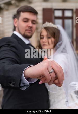 Junge Braut und Bräutigam, zeigen freudig die Ringe. Konzentrieren Sie sich auf Klingelzeichen. Der Kerl und das Mädchen sind verschwommen. Neue Familie, Freude, Liebe, Hochzeit, Eheringe. Stockfoto