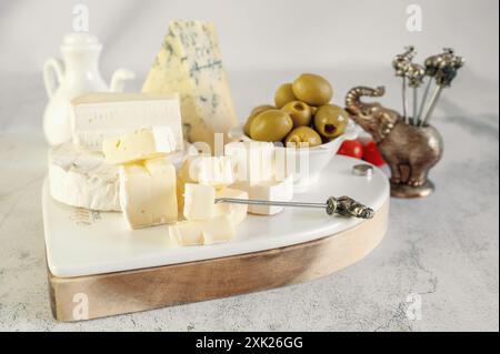 Köstlicher weißer Weichkäse mit Oliven auf einer originalen herzförmigen Käseplatte. Eine Auswahl an Käsesorten mit weißer und blauer Schimmelform auf dem Tisch Stockfoto
