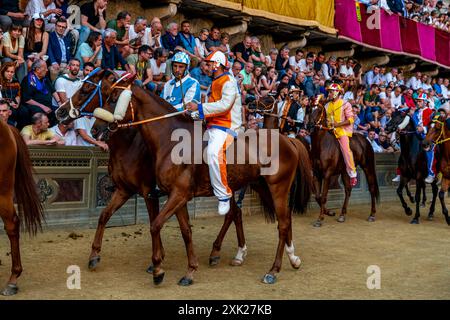 Jockeys in ihren Contrada-Farben machen sich auf den Weg zur Startlinie für das Palio-Rennen. Das Rennen dauert weniger als 90 Sekunden in Siena, Toskana, Italien. Stockfoto