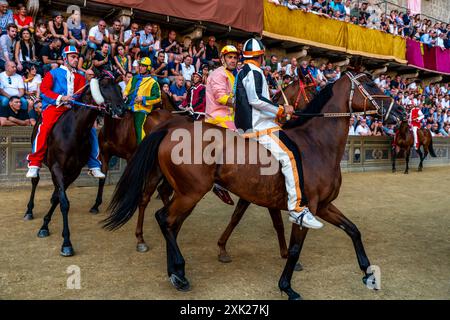 Jockeys in ihren Contrada-Farben machen sich auf den Weg zur Startlinie für das Palio-Rennen. Das Rennen dauert weniger als 90 Sekunden in Siena, Toskana, Italien. Stockfoto