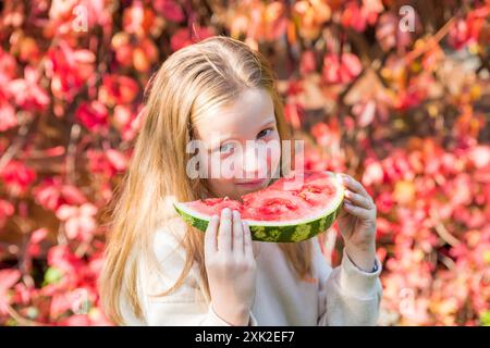 Ein kleines Mädchen mit einem hellen Lächeln im Gesicht hält freudig ein Stück Wassermelone in den Händen. Sommerkonzept. Stockfoto