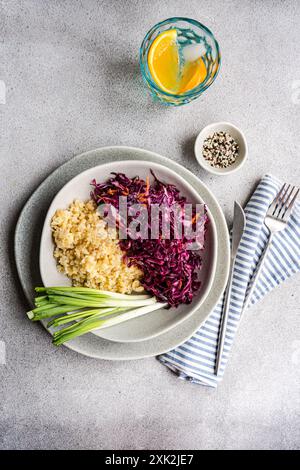 Teller mit gesunden Speisen mit flauschigem gekochtem Bulgur, kombiniert mit einem bunten rohen Rotkohl- und Karottensalat, ergänzt durch frische grüne Zwiebeln und Stockfoto