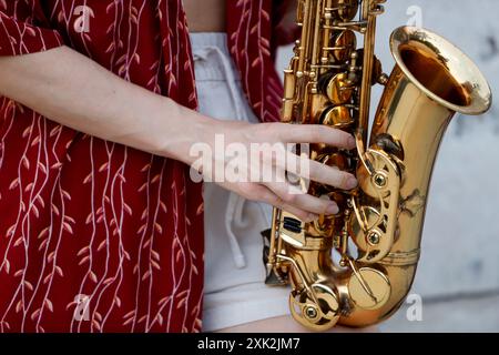 Eine detaillierte Nahaufnahme von anonymen Frauenhänden, die geschickt ein glänzendes goldenes Saxophon spielen, mit einem Blick auf ein rot gemustertes Kleid, das das B betont Stockfoto