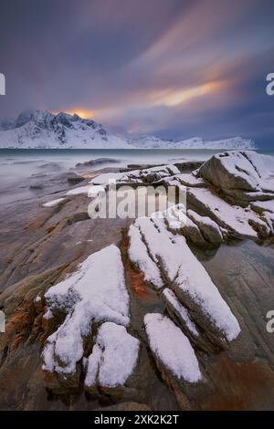 Majestätische, schneebedeckte Gipfel erheben sich über dem Meer unter dem Dämmerungshimmel in Lofoten. Schneebedeckte Felsen und eiskaltes Wasser verschmelzen zu einer ruhigen Szene, die die se vermittelt Stockfoto