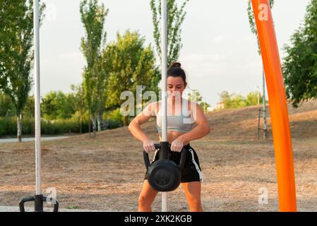 Eine fokussierte junge Frau trainiert an einem klaren Tag Gewichte in einem örtlichen Straßenstudio und zeigt eine Outdoor-Fitness-Routine Stockfoto