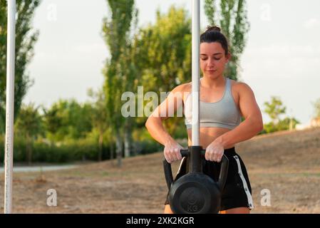 Eine fokussierte junge Frau trainiert an einem klaren Tag Gewichte in einem örtlichen Straßenstudio und zeigt eine Outdoor-Fitness-Routine Stockfoto