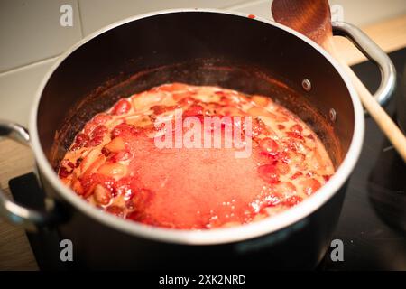 Nahaufnahme eines schwarzen Topfes mit Erdbeermarmelade, die während der Zubereitung kocht. Stockfoto
