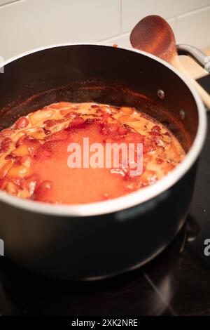 Nahaufnahme eines schwarzen Topfes mit Erdbeermarmelade, die während der Zubereitung kocht. Vertikale Aufnahme. Stockfoto