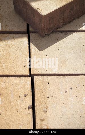 Detaillierte Aufnahme eines großen Steins auf beigen Fliesen mit gegossenem Schatten und verstreuten kleinen Kieselsteinen. Stockfoto