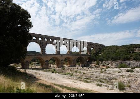 VERS-PONT-DU-GARD, Frankreich – der majestätische Pont du Gard, ein altes römisches Aquädukt und UNESCO-Weltkulturerbe, erstreckt sich über den ruhigen Fluss Gardon in Südfrankreich. Diese bemerkenswerte dreistöckige Brücke zeigt den Einfallsreichtum römischer Technik vor dem Hintergrund der malerischen mediterranen Landschaft. Stockfoto