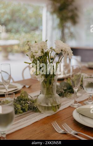 Ein eleganter Tisch mit floralem Herzstück in einer Glasvase, bereit für einen besonderen Anlass. Stockfoto