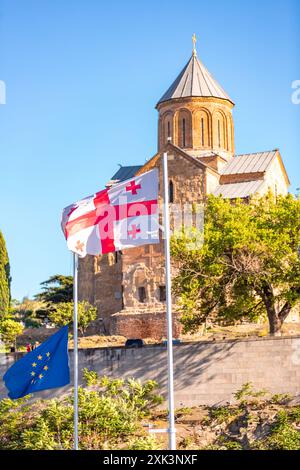 Georgische und EU-Fahnen winken vor der Kirche der Geburt der Mutter Gottes in Metekhi, die sich am linken Ufer des Flusses Kura in Tiflis befindet. Stockfoto