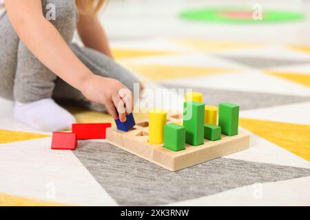 Kleines Mädchen, das mit geometrischen Holzfiguren auf dem Teppich spielt, Nahaufnahme. Kindergartenaktivitäten zur motorischen Entwicklung Stockfoto