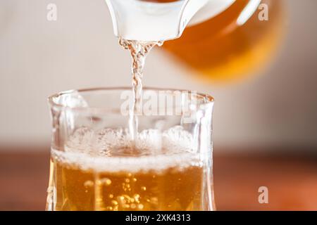 Ein Glas, das mit einem goldenen Getränk gefüllt wird, möglicherweise Bier, mit Blasen, die sich oben bilden. Der Hintergrund ist sanft verschwommen und betont das Getränk b Stockfoto