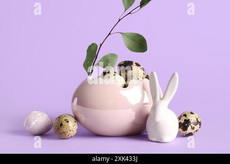 Dekorativer Korb mit Osterwachteleiern, Häschen- und Eukalyptuszweig auf lila Hintergrund Stockfoto