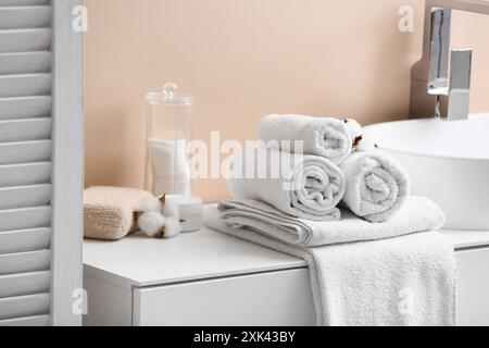 Saubere, weiche Handtücher, Halter mit Wattepads und Baumwollblumen auf dem Tisch in der Nähe der beigefarbenen Wand im Badezimmer Stockfoto