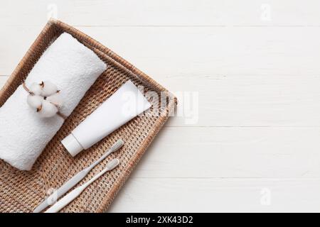 Schöne Komposition mit Korb, gerolltes weiches Handtuch, Mundpflege-Set und Baumwollblume auf weißem hölzernem Hintergrund, Großansicht Stockfoto