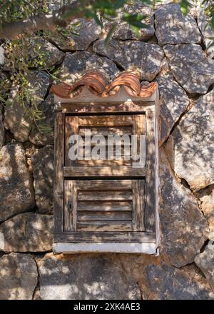 Altes, kleines Fenster mit Holzläden, Jalousien in einer Wand aus großem Stein Stockfoto