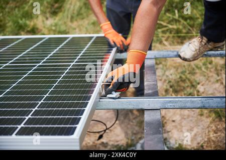 Nahaufnahme von männlichen Arbeitern in Handschuhen, die Solarpaneele auf Metallschienen montieren. Männer-Hand-Montage des Solarmoduls zur Stromerzeugung durch Photovoltaik-Effekt. Konzept der erneuerbaren Energiequellen. Stockfoto