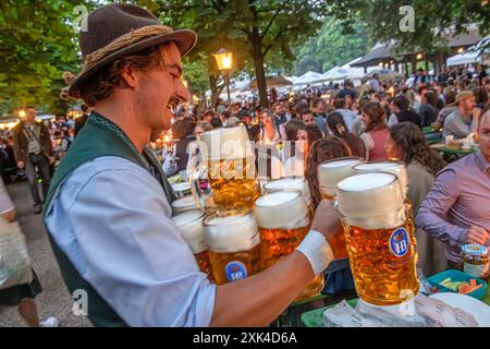 Kocherlball am Chinesischen Turm, Bedienung bringt Gäste 10 Maß Bier, morgens um 5:20 Uhr, München, 21. Juli 2024 Deutschland, München, 21. Juli 2024, Biertrinken bei Kerzenschein, Kocherlball am Chinesischen Turm, Englischer Garten, Bedienung bringt Gäste 10 Maß Bier, morgens um 5:20 Uhr, Besucher feiern früh morgens, halb in der Nacht, sitzen schon teilweise ab 4 Uhr früh im Biergarten, trinken ein Bier, essen eine Brotzeit, tragen Tracht, Tradition entstand im 19. Jahrhundert, als Hauspersonal, Dienstboten und Köchinnen in den frühen Morgenstunden vor Dienstbeginn feiern und getanzt hab Stockfoto