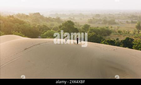 Aus der Vogelperspektive einer Bauernfrau trägt einen Bambusrahmen auf der Schulter über Sanddünen in der Provinz Ninh Thuan, Vietnam. Es ist eines der schönsten Stockfoto