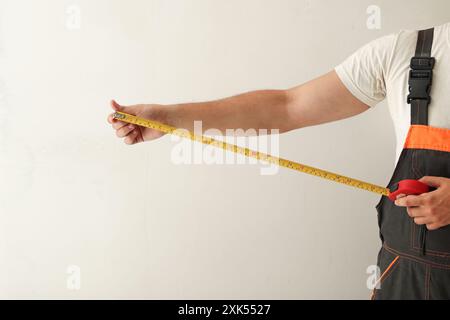 Maßprofil für Handband. Bauarbeiter, der Wand mit Bandmaß misst, weißer Hintergrund. Stockfoto