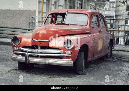 Altes verlassenes Auto in der Stadt. Orange GAZ M20 ohne Scheinwerfer und halbe Windschutzscheibe. Beschädigtes Auto mit Platten Reifen. Stockfoto