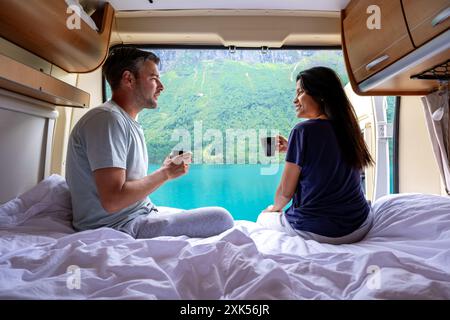 Ein Paar genießt Kaffee und einen malerischen Blick auf einen norwegischen Fjord vom Bett ihres Wohnwagens. Ein vielfältiges Paar Männer und Frauen und ein Mobilheim im Lovatnet Lake Lodal Valley Norwegen Stockfoto