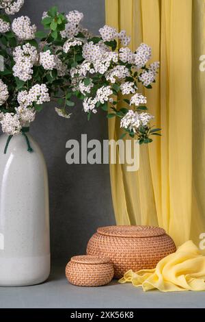 Stillleben mit weißen Blumen, Spirea. Zweige weißer Blüten in einer braunen Vase auf grauem Hintergrund, neben zwei runden Körben. Viele Orte für Tex Stockfoto