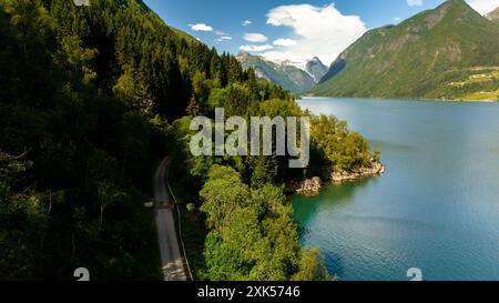 Eine gewundene Straße führt durch üppige grüne Vegetation in Richtung eines ruhigen Fjords, eingebettet zwischen majestätischen Bergen. Fjaerlandsfjorden, Fjord, Vestland, Norwegen Stockfoto