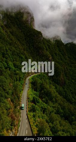 Ein einsames Auto fährt auf einer kurvenreichen Straße durch dichte Wälder und nebelige Berge in Norwegen. Lovrafjorden, Norwegen Stockfoto