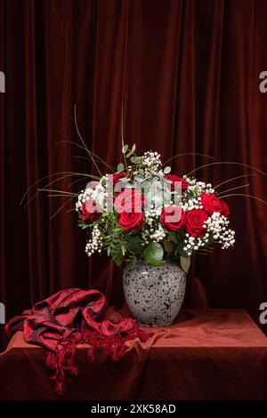 Ein riesiger Strauß roter Rosen mit weißen Blumen auf einem dunkelbraunen Stoff. Stillleben. Stockfoto