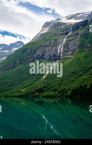 Ein majestätischer Wasserfall stürzt einen grünen Berghang hinunter, dessen Reflexion die Schönheit im stillen Wasser eines ruhigen Sees widerspiegelt. Lovatnet See Lodal Tal Norwegen Stockfoto