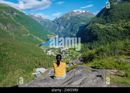 Eine Frau sitzt auf einem felsigen Felsvorsprung mit Blick auf einen atemberaubenden norwegischen Fjord und genießt die Schönheit der grünen Berge und des blauen Wassers. Geiranger Fjord Norwegen Stockfoto