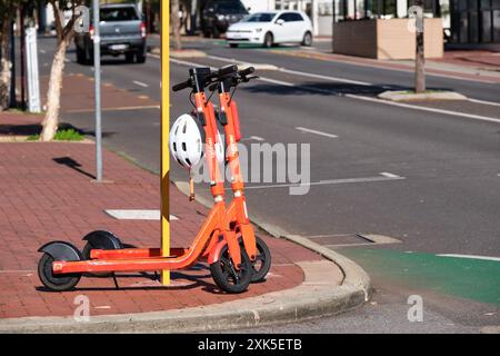 Zwei orangefarbene Neuron Mobility E-Scooter mit Helmen zur Miete an einer Straßenecke im inneren Vorort von Leederville, Perth, Western Australia. Stockfoto