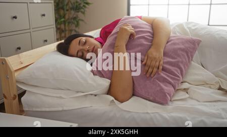 Frau, die bequem auf ihrem Bett schläft, während sie ein weiches rosafarbenes Kissen in einem gemütlichen Schlafzimmer umschließt. Stockfoto