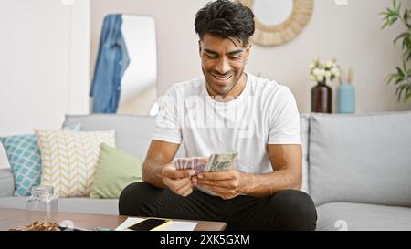 Lächelnder junger Mann, der polnische Zloty in gemütlicher Wohnzimmereinrichtung zählt. Stockfoto