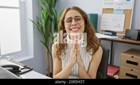 Eine junge hispanische Frau lächelt in einem modernen Büroumfeld mit Händen und strahlt Charme und Professionalität aus Stockfoto