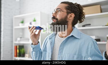 Hispanischer Mann mit Bart mit Sprachassistent am Smartphone im modernen Büro Stockfoto