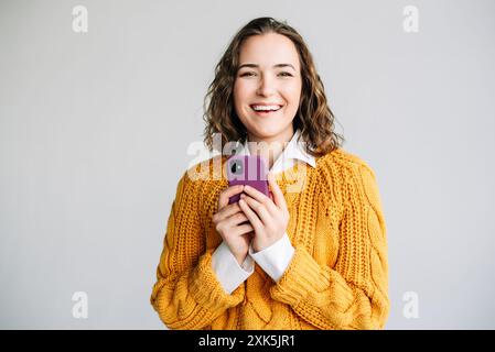 Glückliche Frau Mit Smartphone. Eine fröhliche junge Frau, die ein Smartphone hält, lächelt und aufgeregt aussieht. Perfekt für die Werbung für E-Commerce und Mobilgeräte Stockfoto