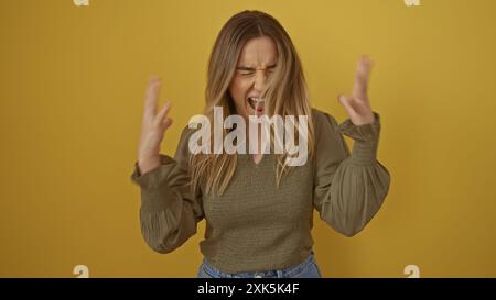 Eine attraktive junge Frau brüllt frustriert vor einer isolierten gelben Hintergrundwand und zeigt ausdrucksstarke Emotionen. Stockfoto