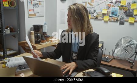 Eine fokussierte blonde Detektivin analysiert Beweise an ihrem Bürotisch, umgeben von Akten und einem Anschlagbrett. Stockfoto