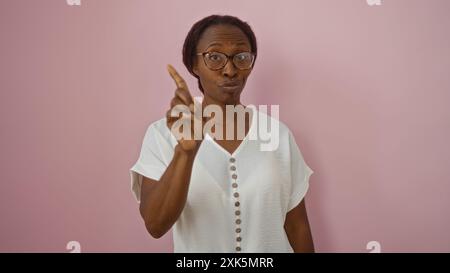 Eine afroamerikanische Frau macht eine Geste ohne Finger vor einem rosa Hintergrund und hält einen Moment der Missbilligung oder Warnung fest. Stockfoto