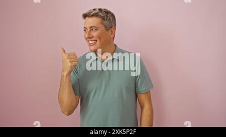 Junger Mann, der lächelnd die Daumen hoch gibt, vor einem rosa Hintergrund steht, isoliert, kaukasisch, erwachsen, attraktiv, gut aussehend, Porträt, Person, männlich Stockfoto
