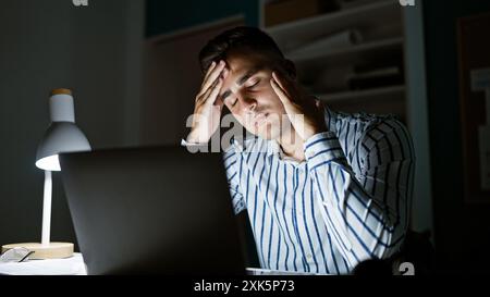 Gestresster junger hispanischer Mann nachts im Büro mit Laptop, Brille, Lampe, Müdigkeit, Geschäft, Arbeit, Kopfschmerzen, mentale Gesundheit, überwältigt Stockfoto