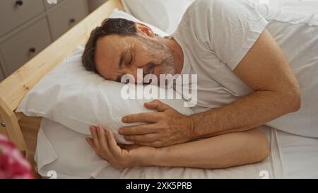 Älterer hispanischer Mann, der friedlich in einem komfortablen Schlafzimmer schläft, zeigt einen Reifen männlichen Mann, der drinnen auf einem Bett ruht. Stockfoto