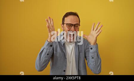 hispanischer Mann mittleren Alters, der Aufregung über isolierten gelben Hintergrund ausdrückt. Stockfoto