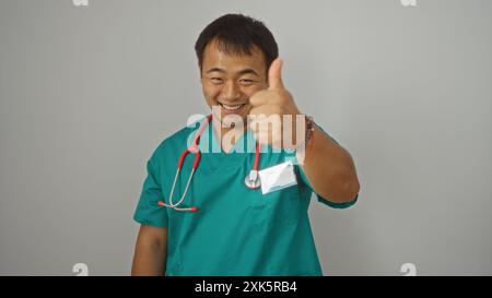 Hübscher chinesischer männlicher Arzt in grünen Peelings, isoliert vor weißem Hintergrund, mit Daumen nach oben und selbstbewusst lächelnd. Stockfoto
