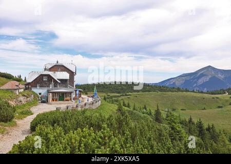 Blick auf das Otto Schutzhaus am Rax, mit dem majestätischen Schneeberg im Hintergrund unter bewölktem Himmel. Die Szene fängt das Idy ein Stockfoto